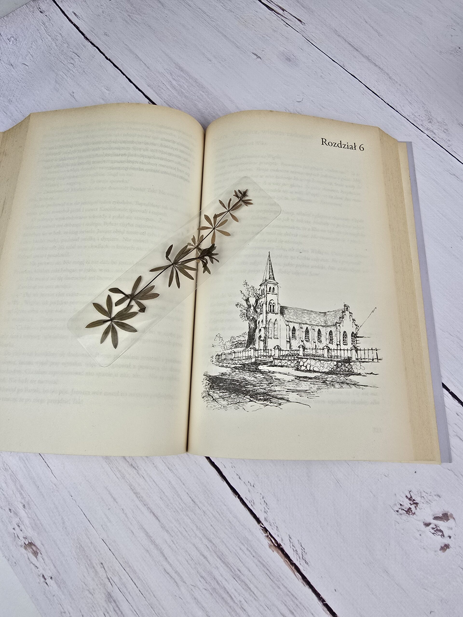 Otwarta książka z zakładką z suszonymi listkami przytulii wonnej i ilustracją kościoła