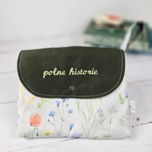 Otulacz na książkę z białej tkaniny w polne kwiaty i zieloną klapką z napisem „polne historie”